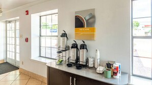 Una zona de recepción con estación de café, una obra de arte con una taza de café enmarcada y una ventana con vistas al exterior.