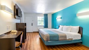 Habitación de hotel con cama, escritorio, silla, televisor y ventana con cortinas.