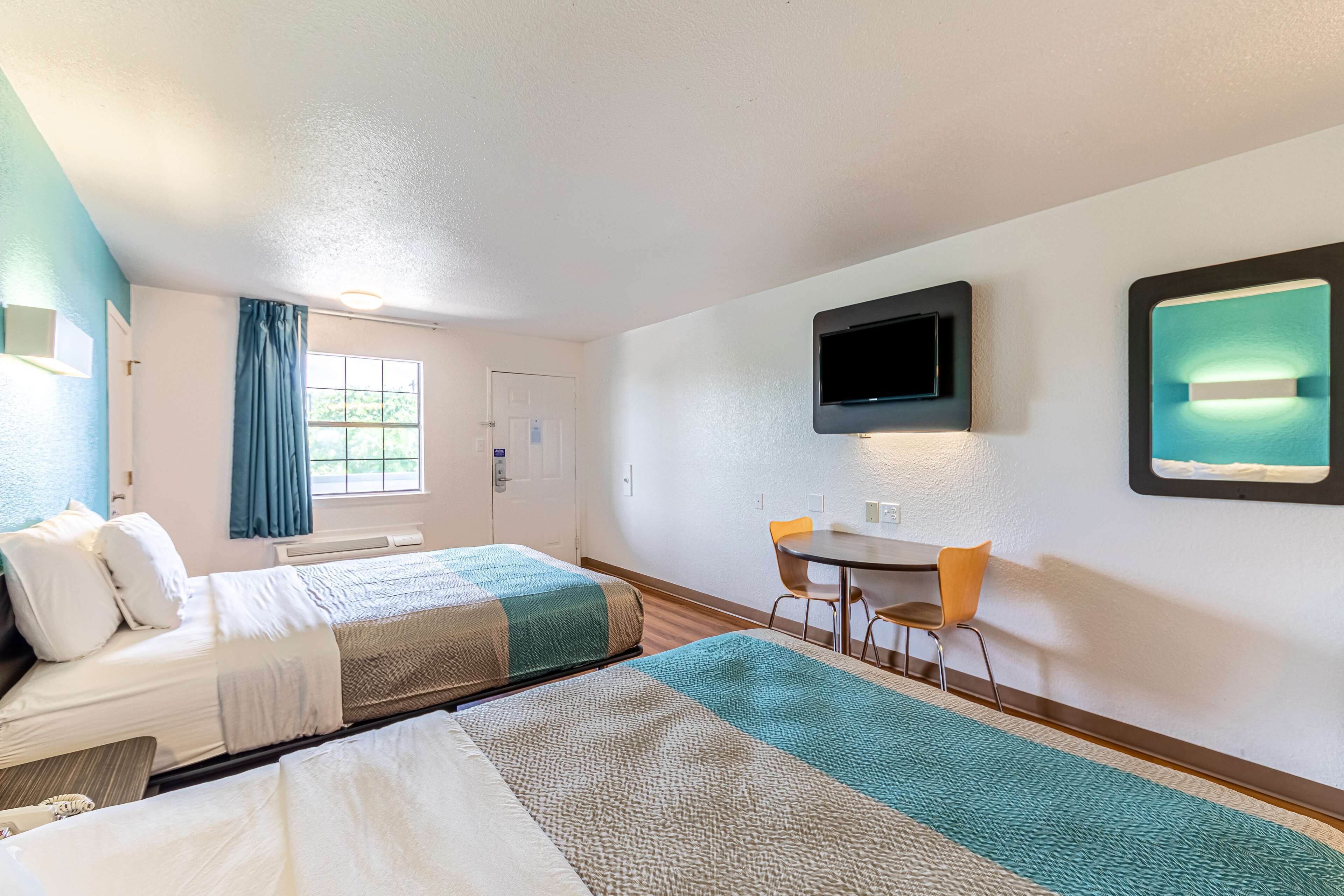 A hotel room with two beds, a desk, a chair, a TV, and a window with curtains.