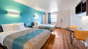 A hotel room with two beds, a dining table, and a TV mounted on the wall.