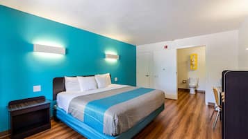 A hotel room with a bed, a nightstand, a bathroom with a toilet, and a door leading to another room.