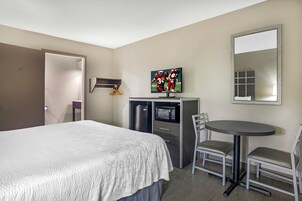 Una habitación de hotel con una cama, un escritorio con silla, un televisor, un refrigerador y un espejo.