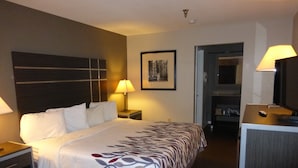 Une chambre d’hôtel comprenant un lit, des tables de chevet, un bureau, une chaise, un miroir, une lampe et un tableau encadré au mur.