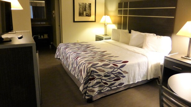 Une chambre d’hôtel avec un lit, des lampes de chevet, un bureau, une chaise et un tableau encadré au mur.