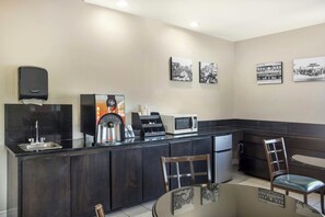 A modern kitchen with a black countertop, stainless steel appliances, a coffee machine, and a seating area with a table and chairs. - Red Roof Inn Columbia, TN (Columbia)