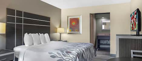A hotel room with a bed, bedside table, lamp, artwork, and a television.