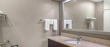 A bathroom with a sink, mirror, towel rack, and toilet paper holder.