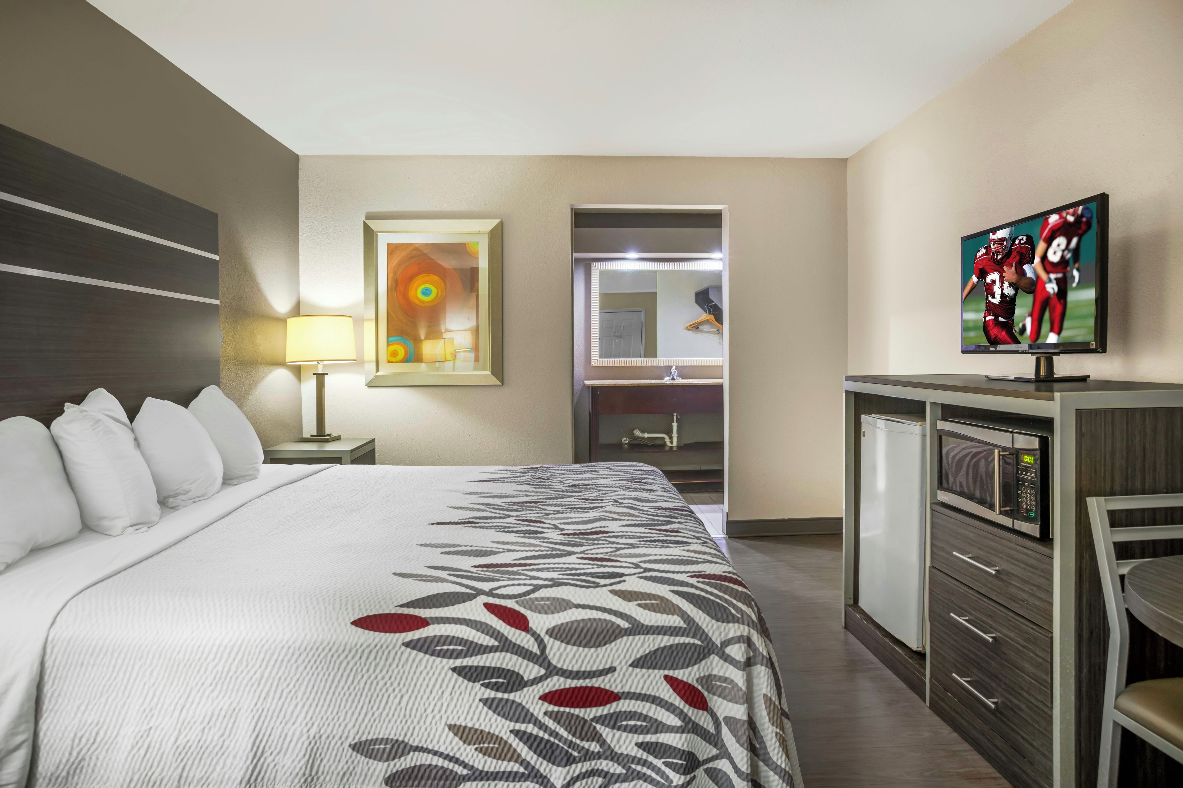 A hotel room with a bed, a desk, a television, and a bathroom visible through an open door.