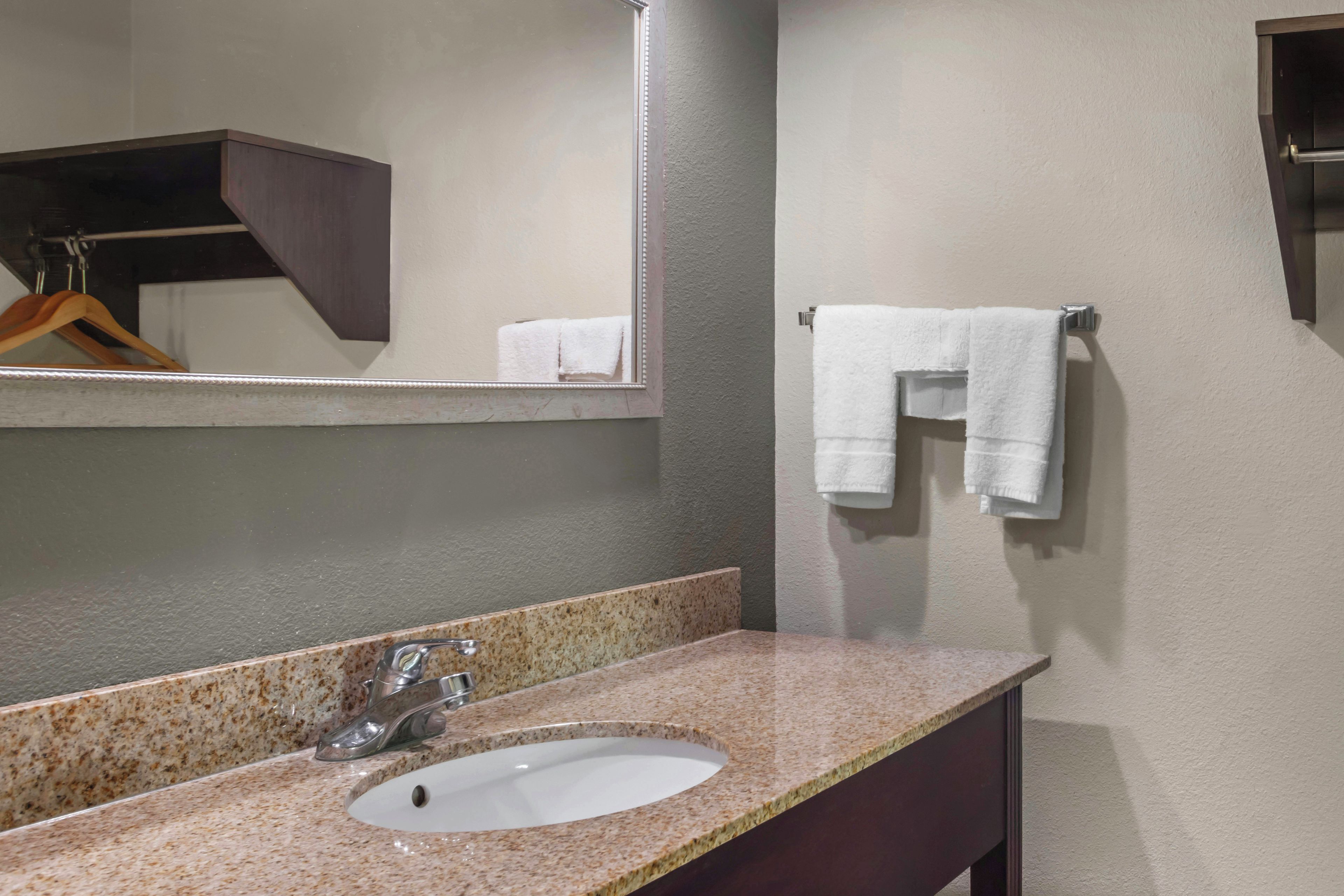 A bathroom with a granite countertop sink, a mirror, and a towel rack with two white towels.