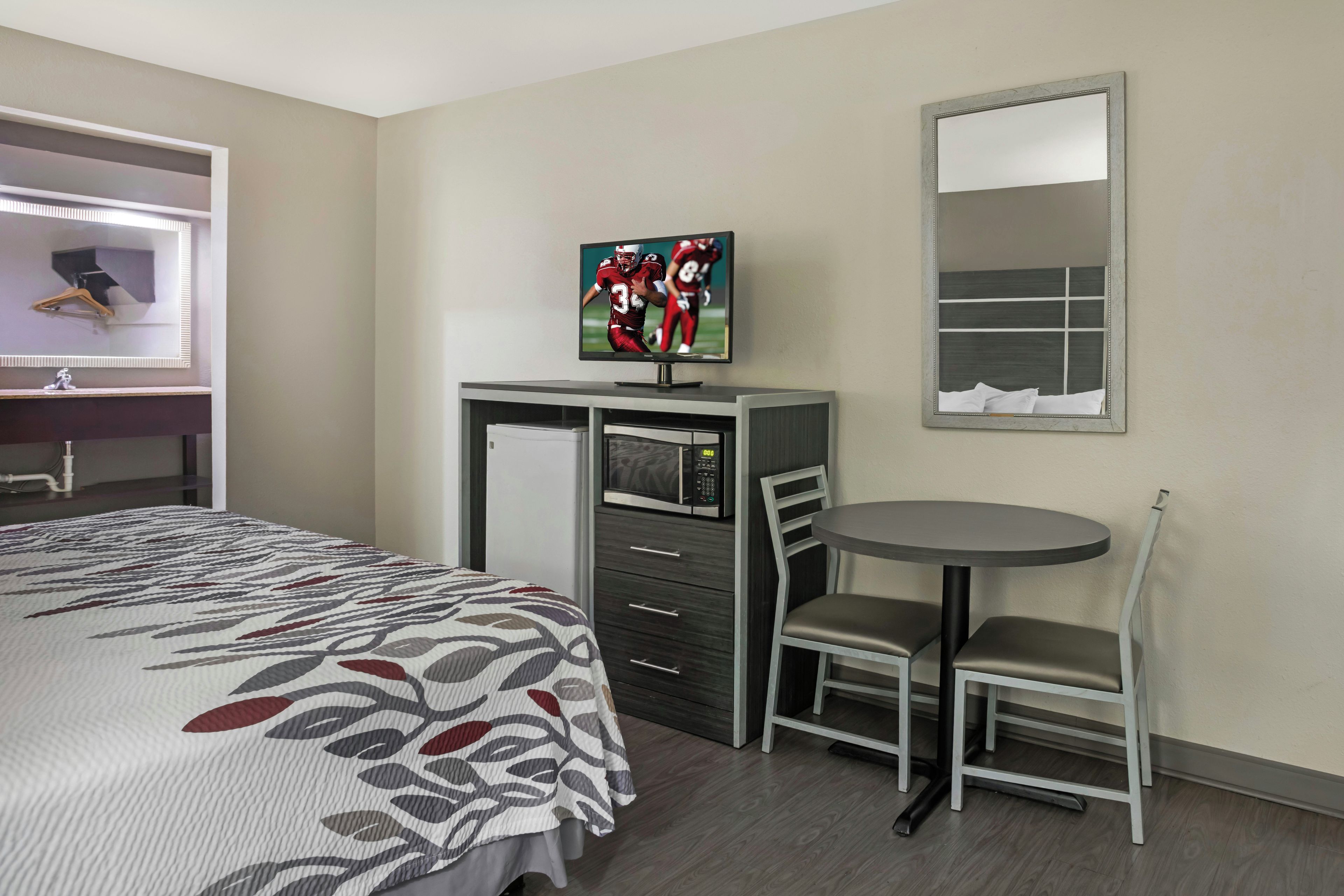 Habitación de hotel con cama, escritorio con televisor, silla, mesita y espejo.