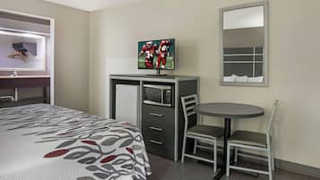 Habitación de hotel con cama, escritorio con televisor, silla, mesita y espejo.