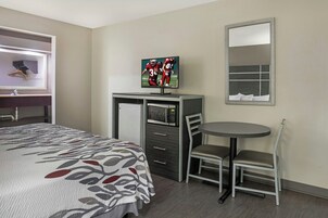 A hotel room with a bed, a desk with a TV, a chair, a small table, and a mirror.