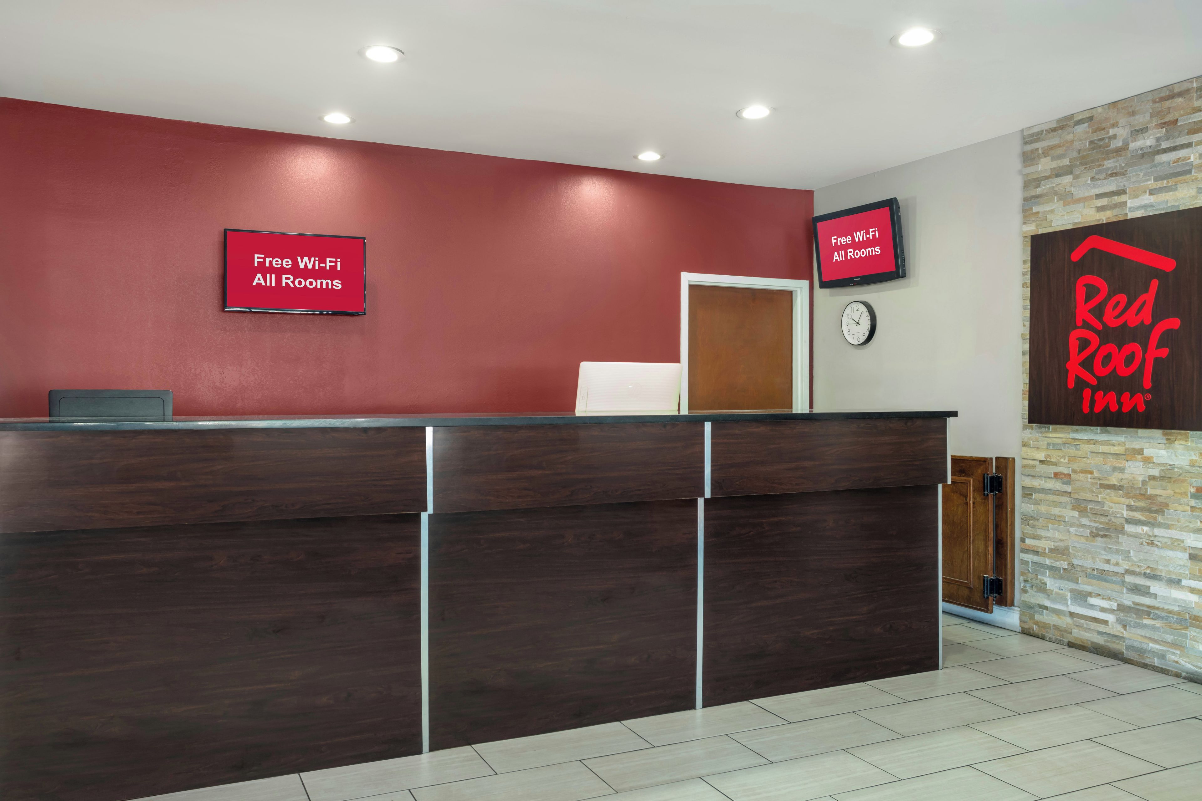 A reception desk with a red wall, a clock, and a sign indicating free Wi-Fi in all rooms.