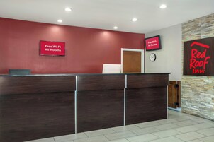 Balcão de recepção com parede vermelha, um relógio e um aviso indicando Wi-Fi gratuito em todos os quartos.