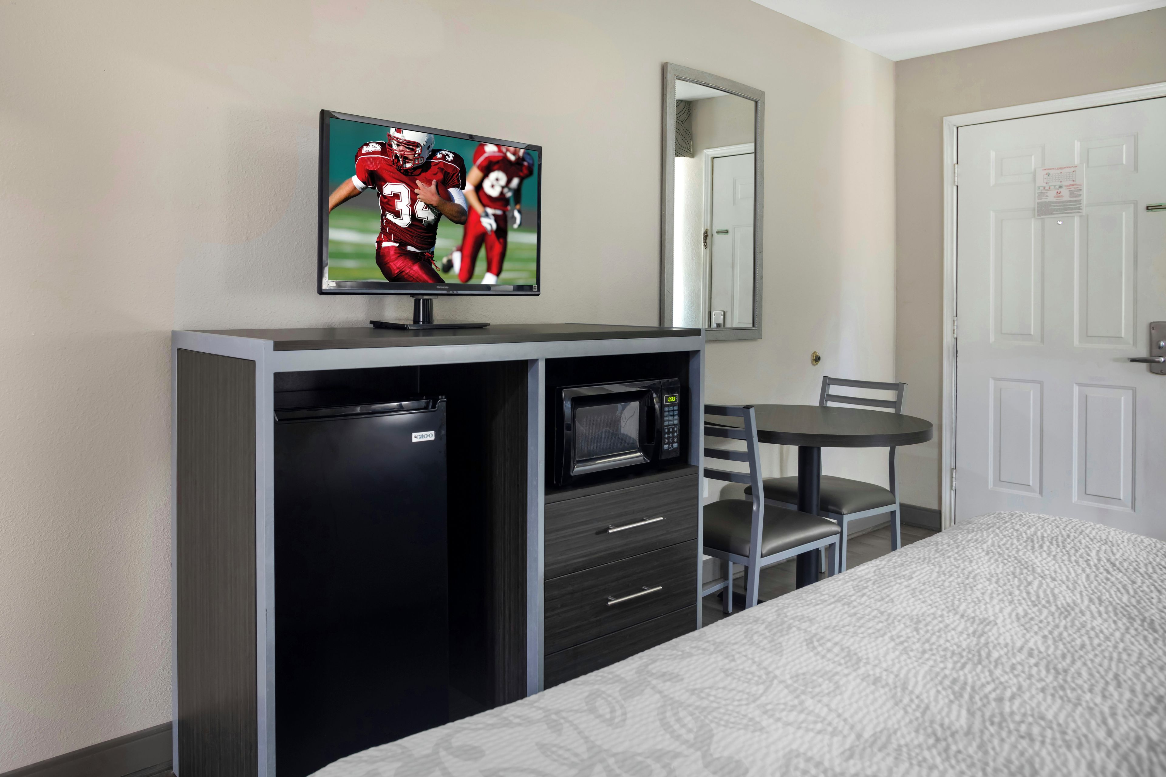 Een hotelkamer met een bed, een televisie bevestigd aan een kast, een magnetron, een kleine koelkast en een stoel.