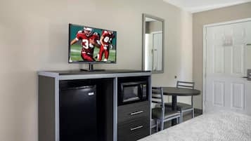 Een hotelkamer met een bed, een televisie bevestigd aan een kast, een magnetron, een kleine koelkast en een stoel.