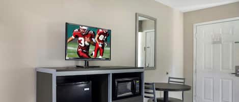 A hotel room with a bed, a TV mounted on a cabinet, a microwave, a small refrigerator, and a chair.