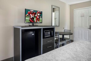 Une chambre d’hôtel équipée d’un lit, d’un téléviseur fixé à un meuble, d’un four à micro-ondes, d’un petit réfrigérateur et d’une chaise.