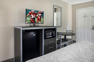 A hotel room with a bed, a TV mounted on a cabinet, a microwave, a small refrigerator, and a chair.