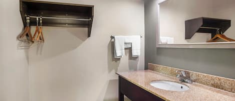 Un baño con lavamanos, espejo, toallero y un perchero de madera.