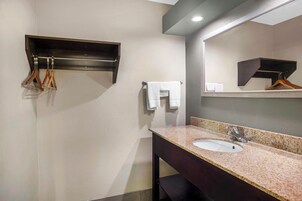 Un baño con lavamanos, espejo, toallero y un perchero de madera.
