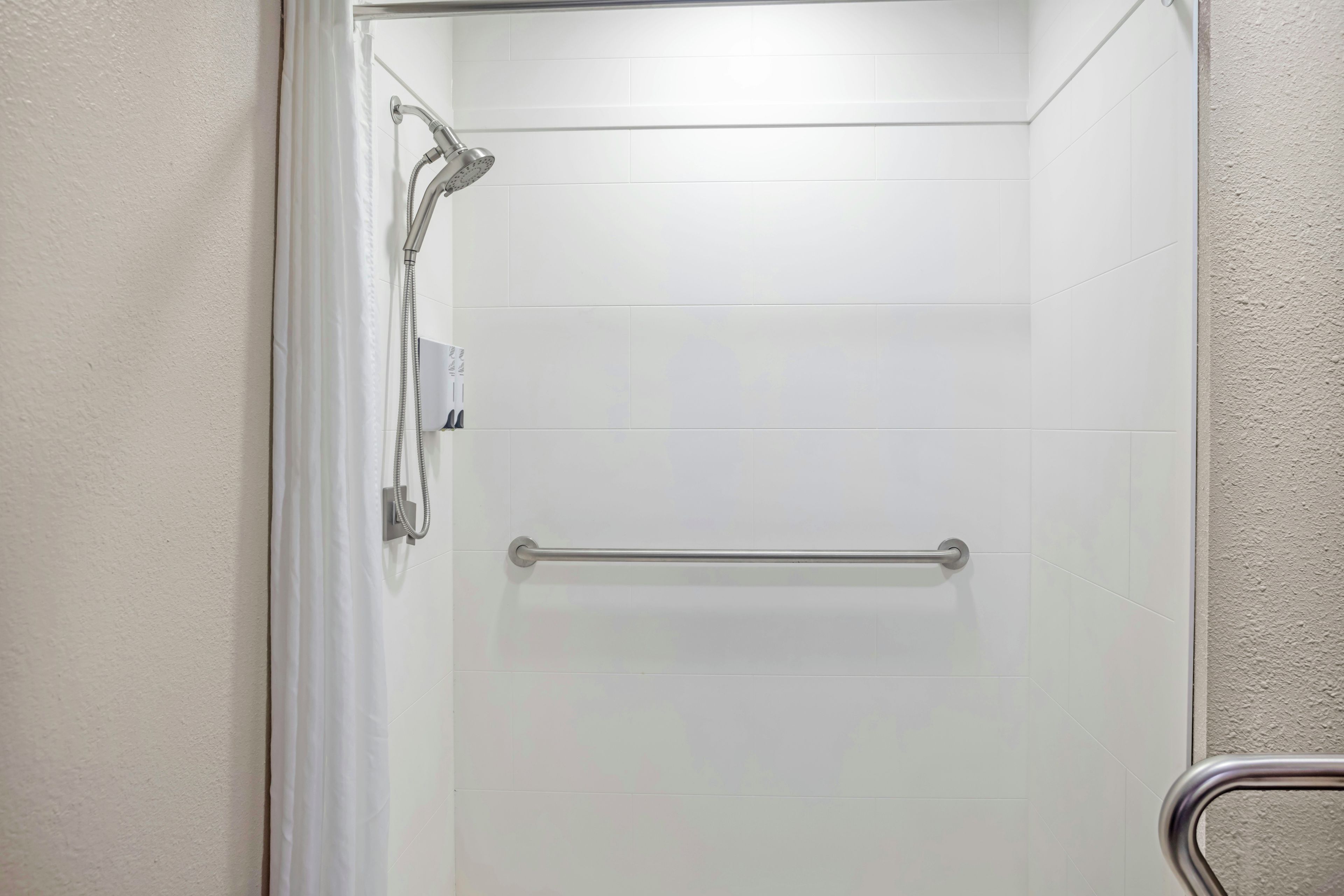 A shower with a handheld showerhead and a grab bar.
