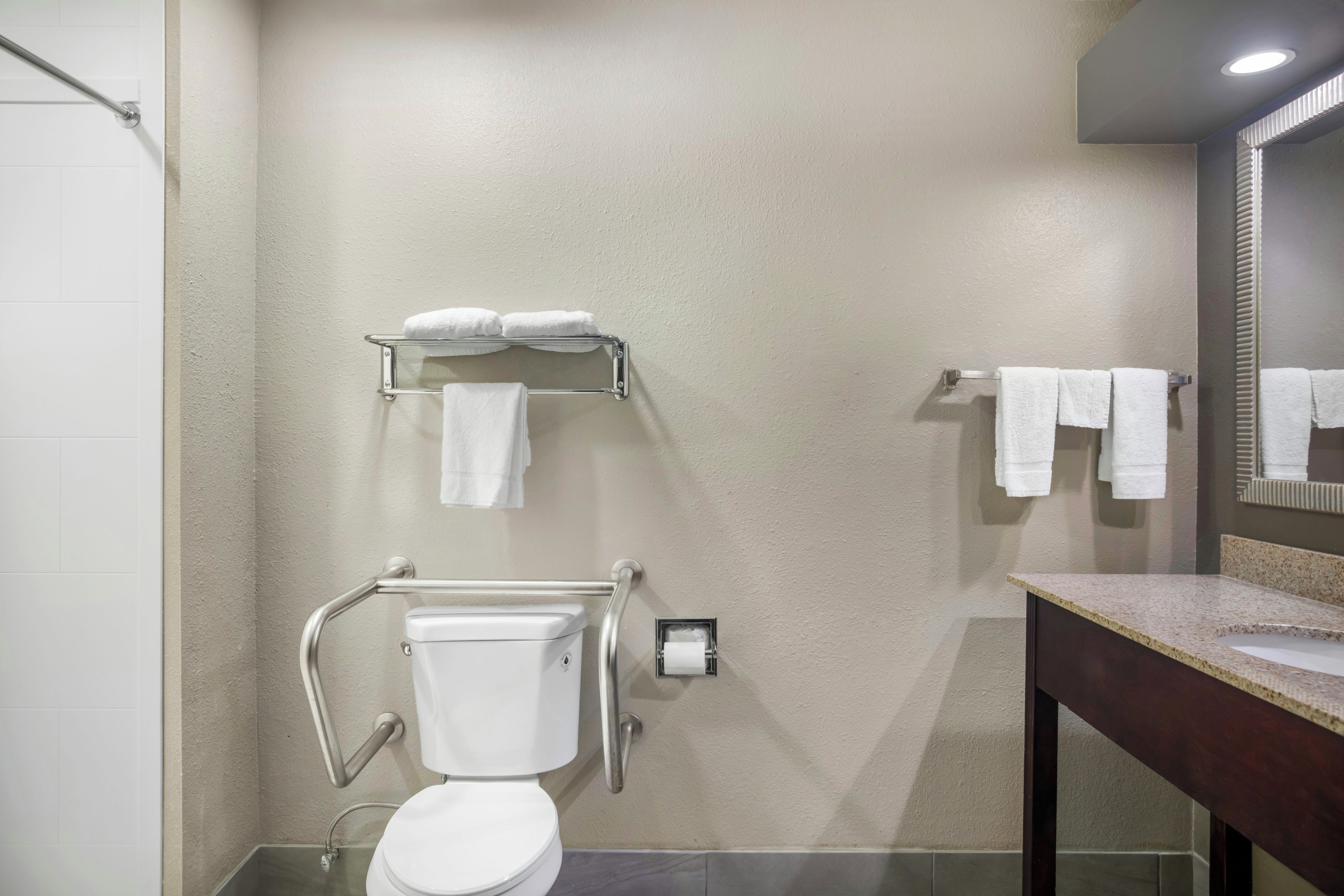 A bathroom with a toilet, grab bars, a towel rack, and a sink.