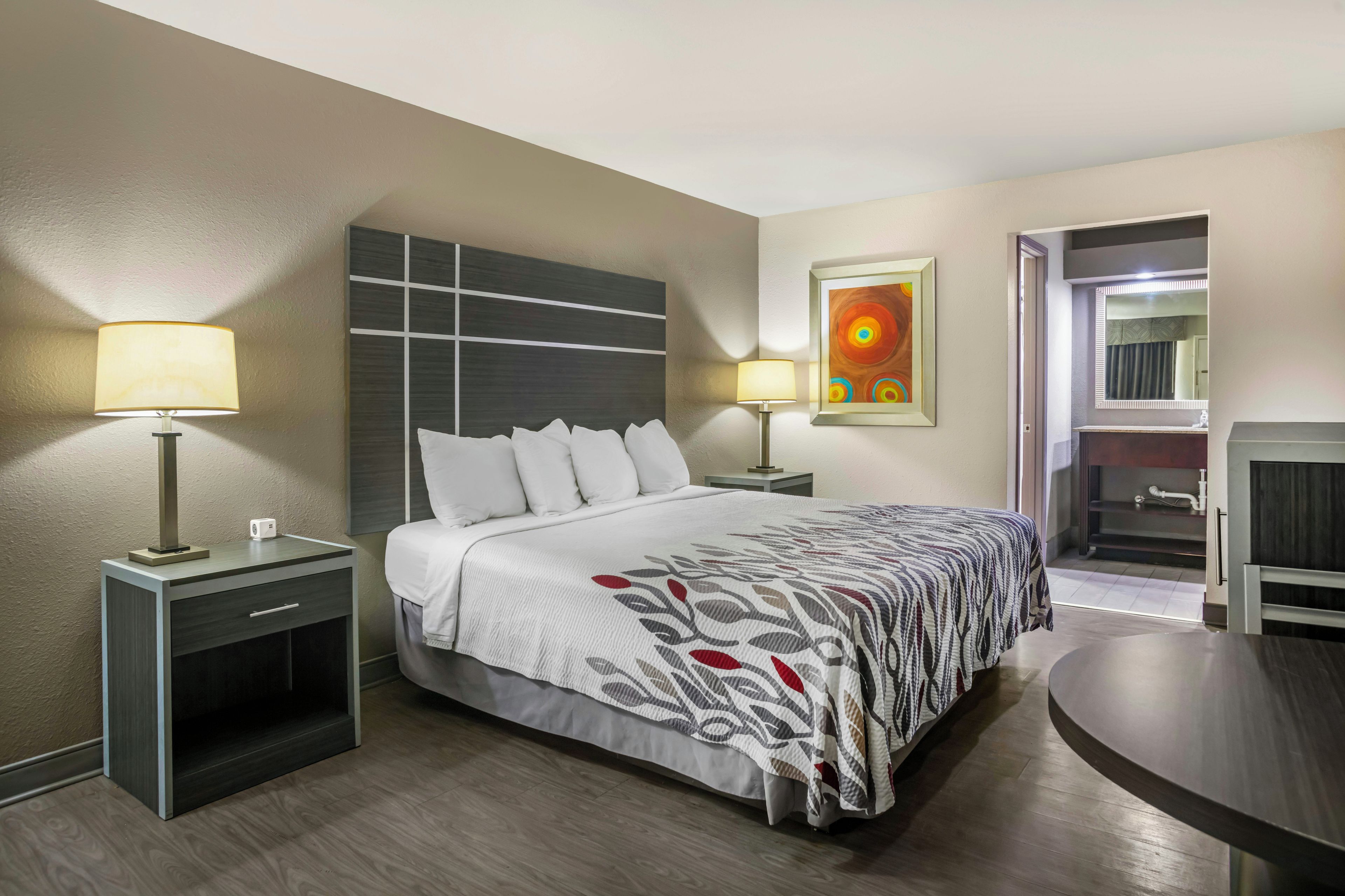 Una habitación de hotel con una cama, dos lámparas de noche, un cuadro, un espejo y una mesita.
