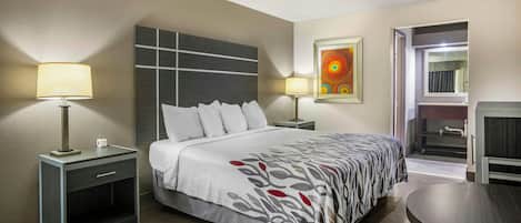 A hotel room with a bed, two bedside lamps, a painting, a mirror, and a small table.