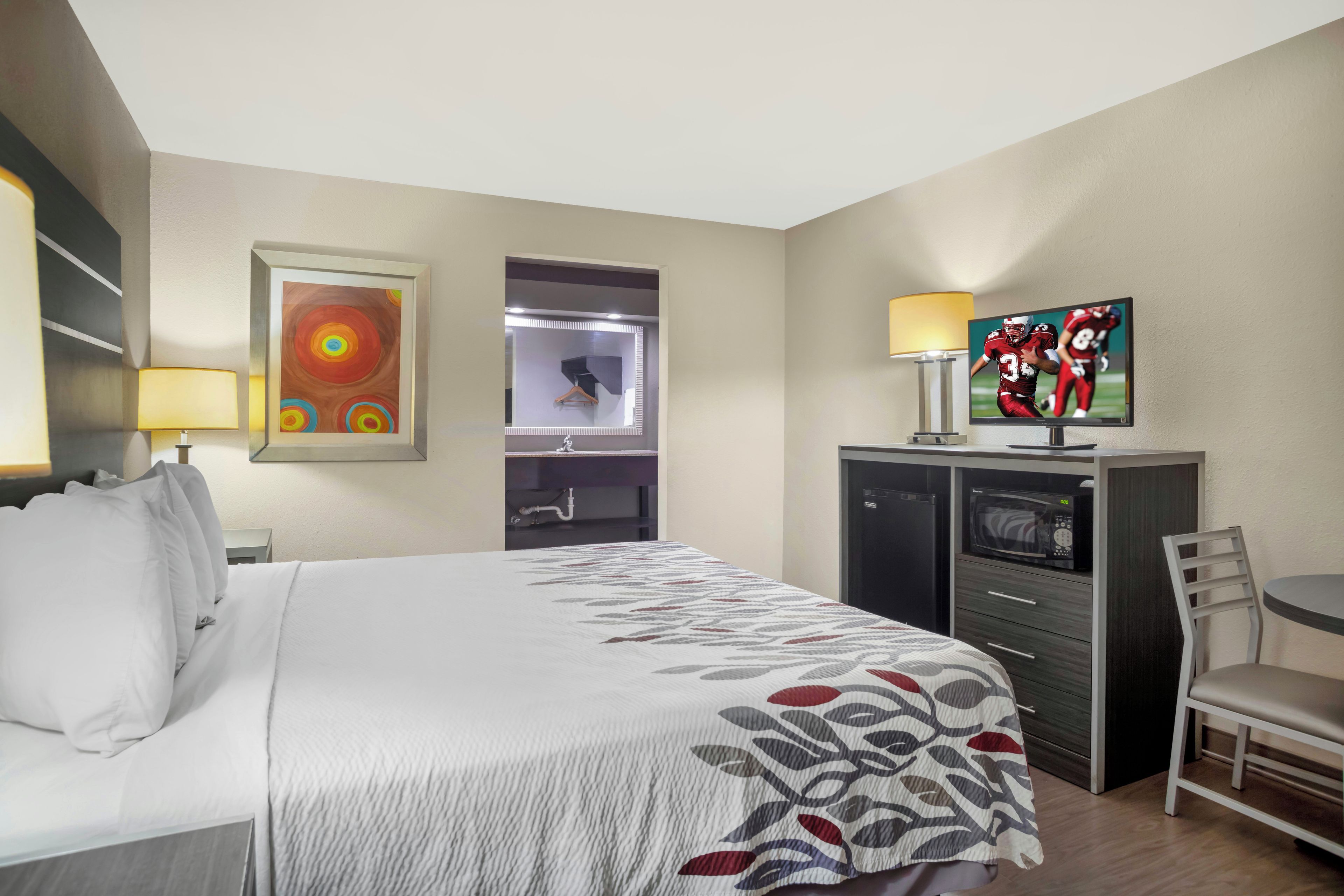 Quarto de hotel com cama, escrivaninha, televisão e micro-ondas.
