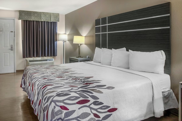A hotel room with a bed, a nightstand, a lamp, a window with curtains, and a door.