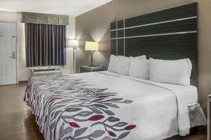 Habitación de hotel con cama, mesita de noche, lámpara, ventana con cortinas y puerta.