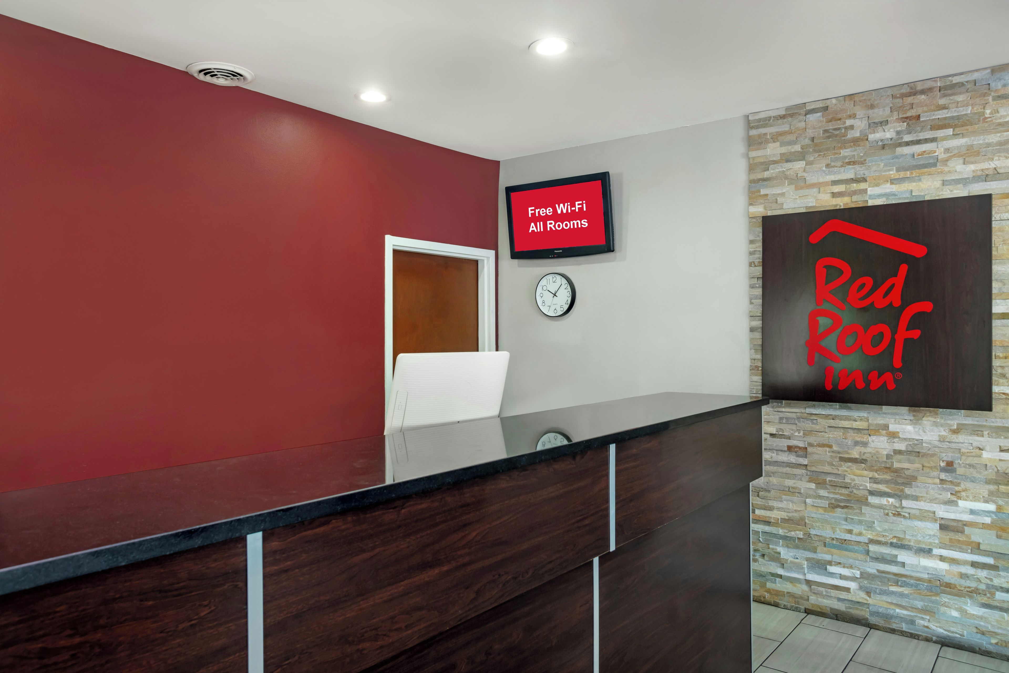 Zona de recepción con una pantalla digital que muestra 'Wi-Fi gratis en todas las habitaciones', un reloj y un letrero de Red Roof Inn.