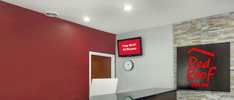 A reception area with a digital screen displaying 'Free Wi-Fi All Rooms,' a clock, and a Red Roof Inn sign.