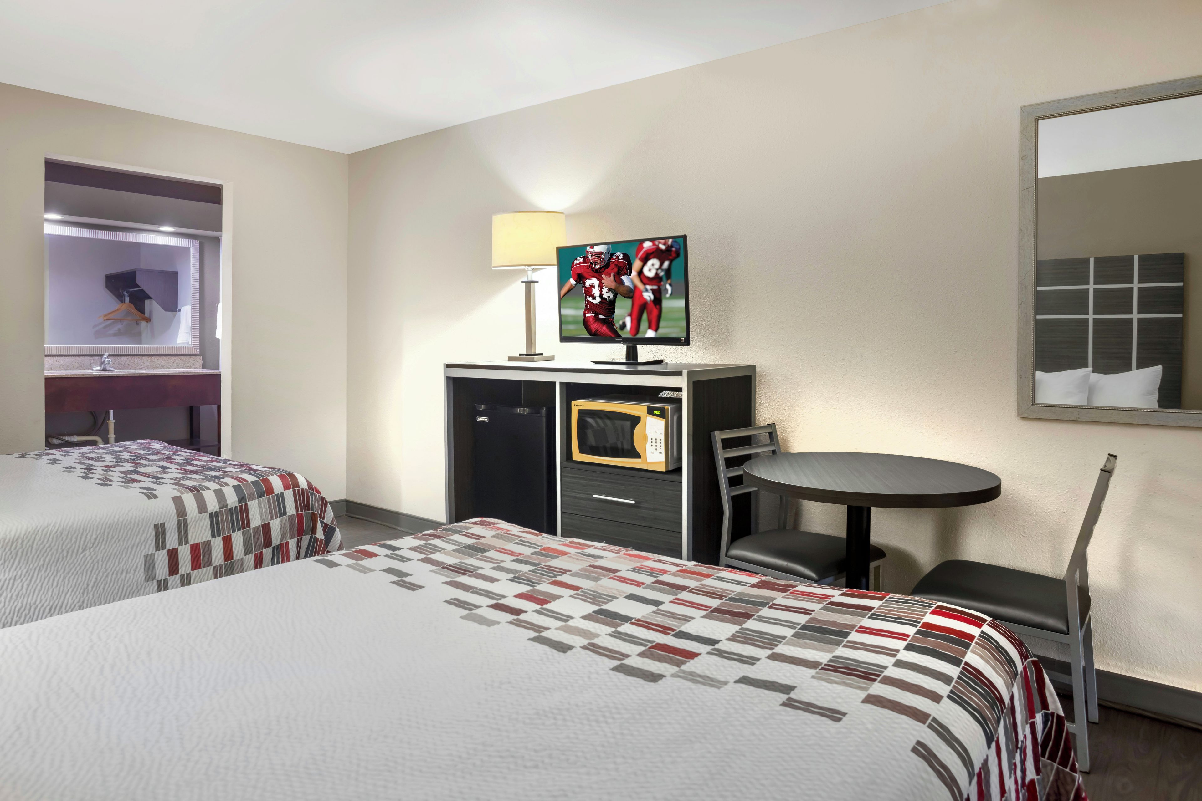 Ett hotellrum med två sängar, ett skrivbord med en tv, ett litet bord och en stol.