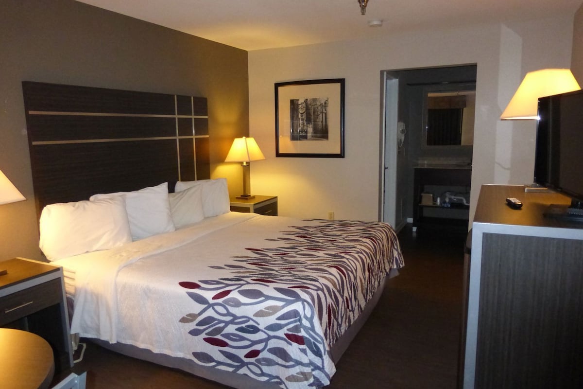 A hotel room with a bed, bedside tables, a desk, a chair, a mirror, and a television.