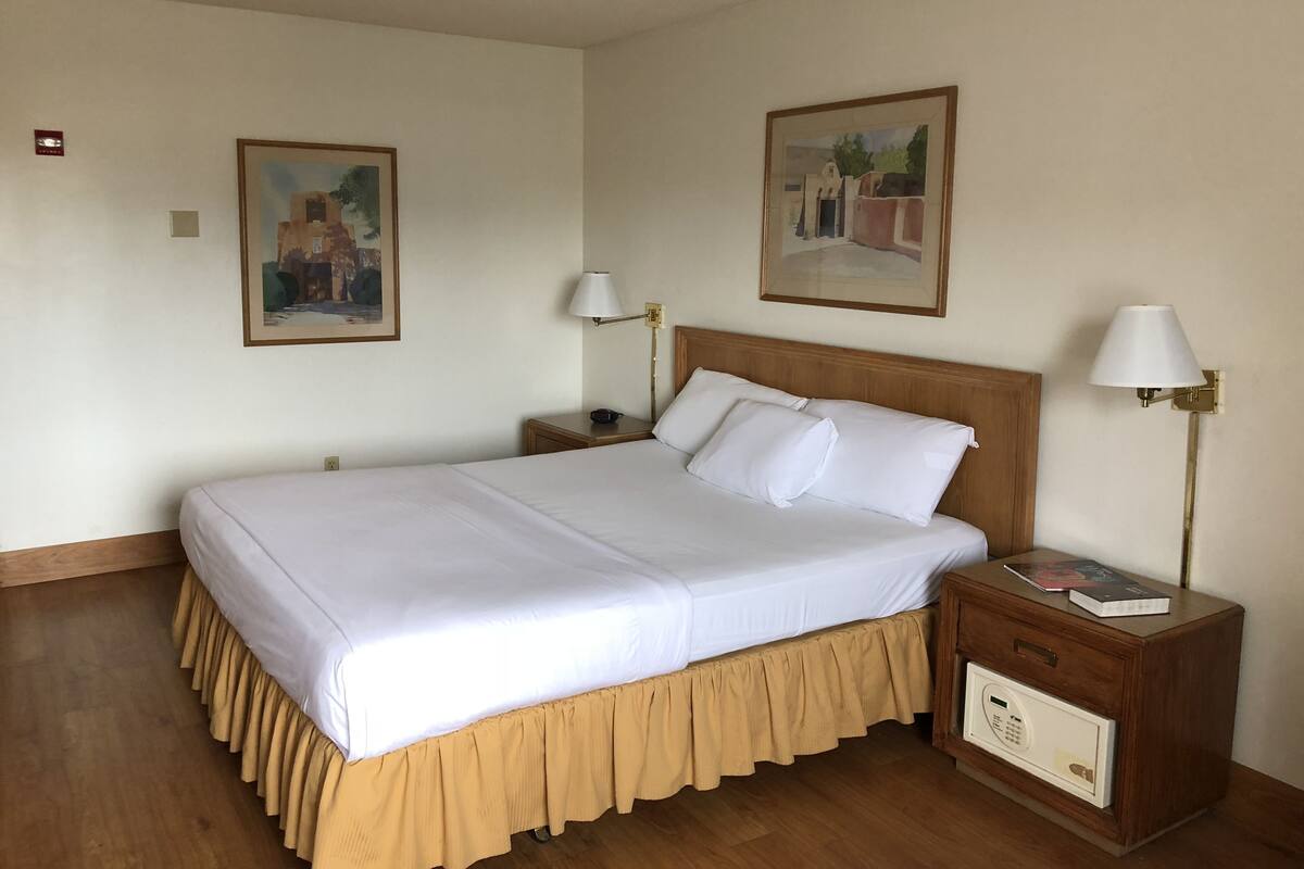 A neatly made bed with white linens and a wooden headboard, flanked by two bedside tables with lamps and a small bedside drawer.
