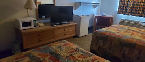 A hotel room with a bed, a desk with a television, a microwave, a refrigerator, and a window with curtains.