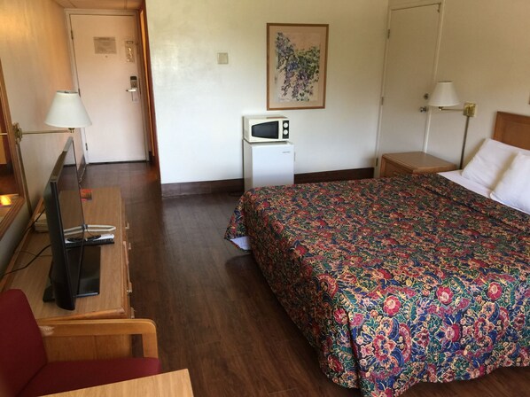 A hotel room with a bed, a desk with a computer, a microwave, and a TV.