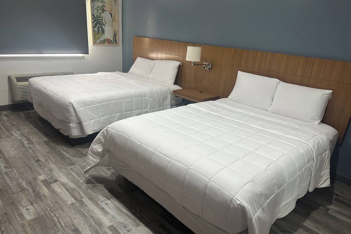 Two single beds with wooden headboards, a nightstand, a wall-mounted lamp, and a vent.