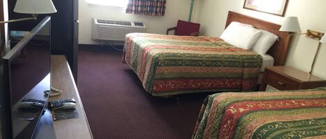 A hotel room with two beds, a desk with a computer, a TV, and a window with curtains.
