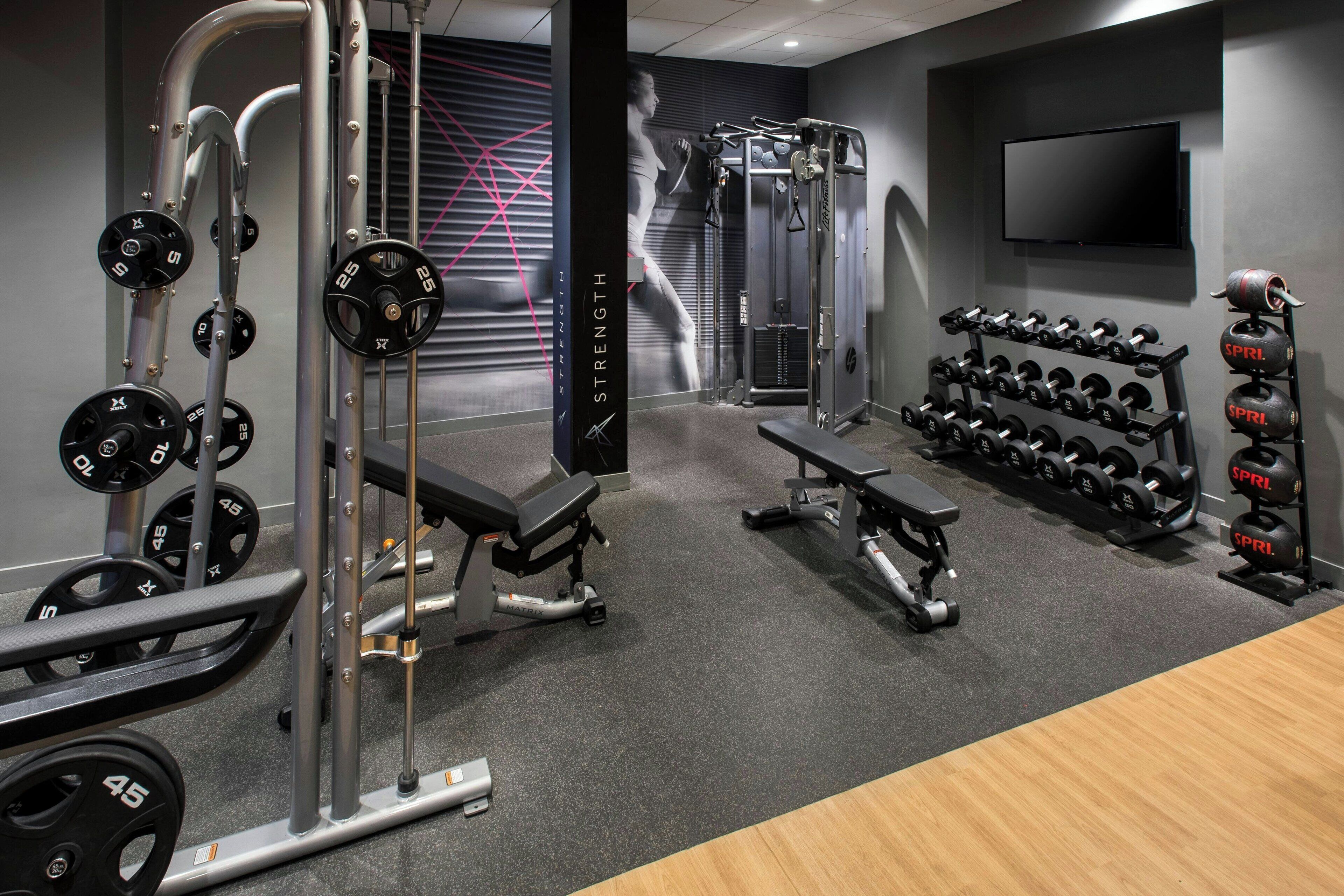 A gym with weightlifting equipment, benches, and a TV mounted on the wall.