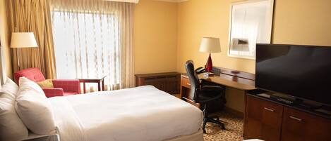 A hotel room with two beds, a desk with a television, a chair, and a window with curtains.