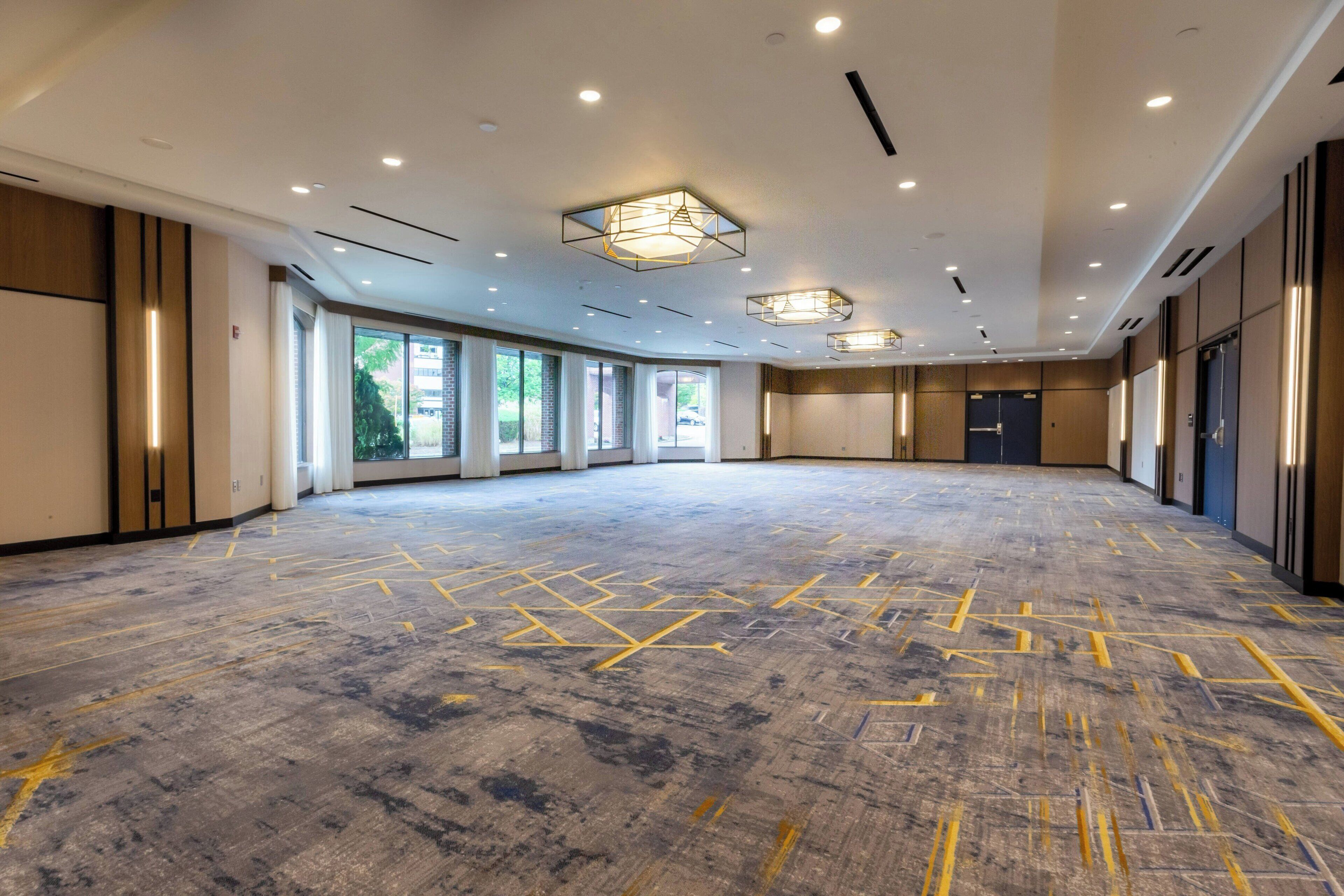 A spacious, well-lit conference room with a patterned floor, large windows, and modern lighting fixtures.