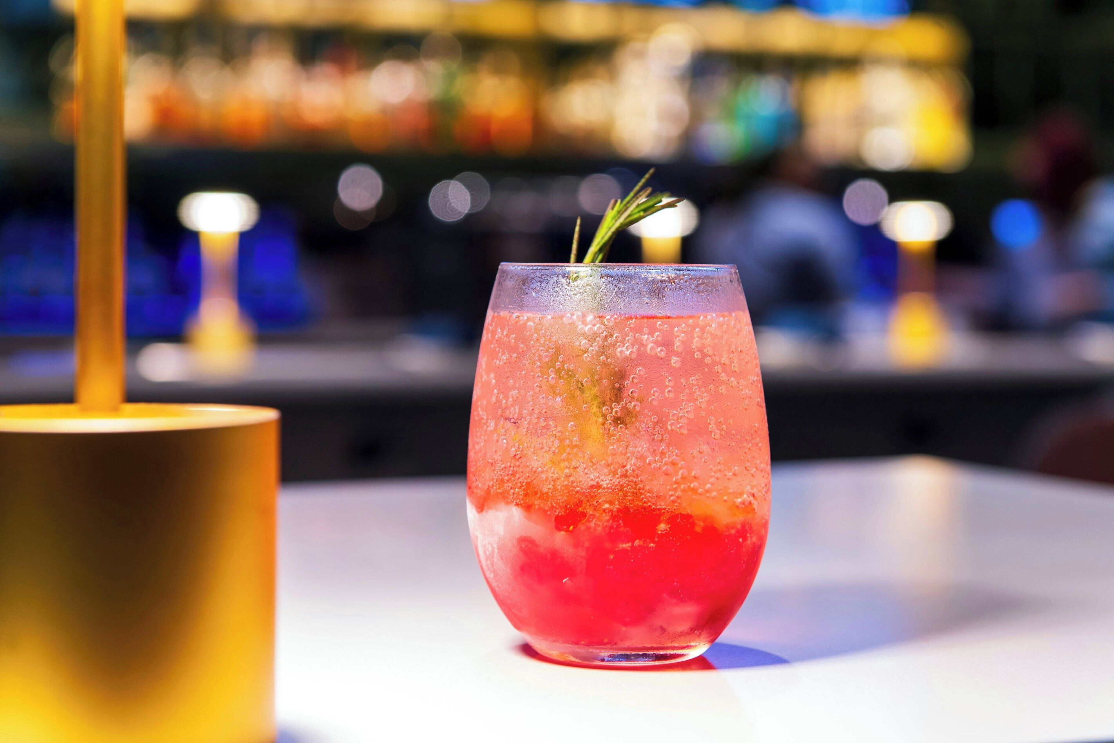 Ein Cocktailglas mit Rosmarinzweig auf einer Bar.
