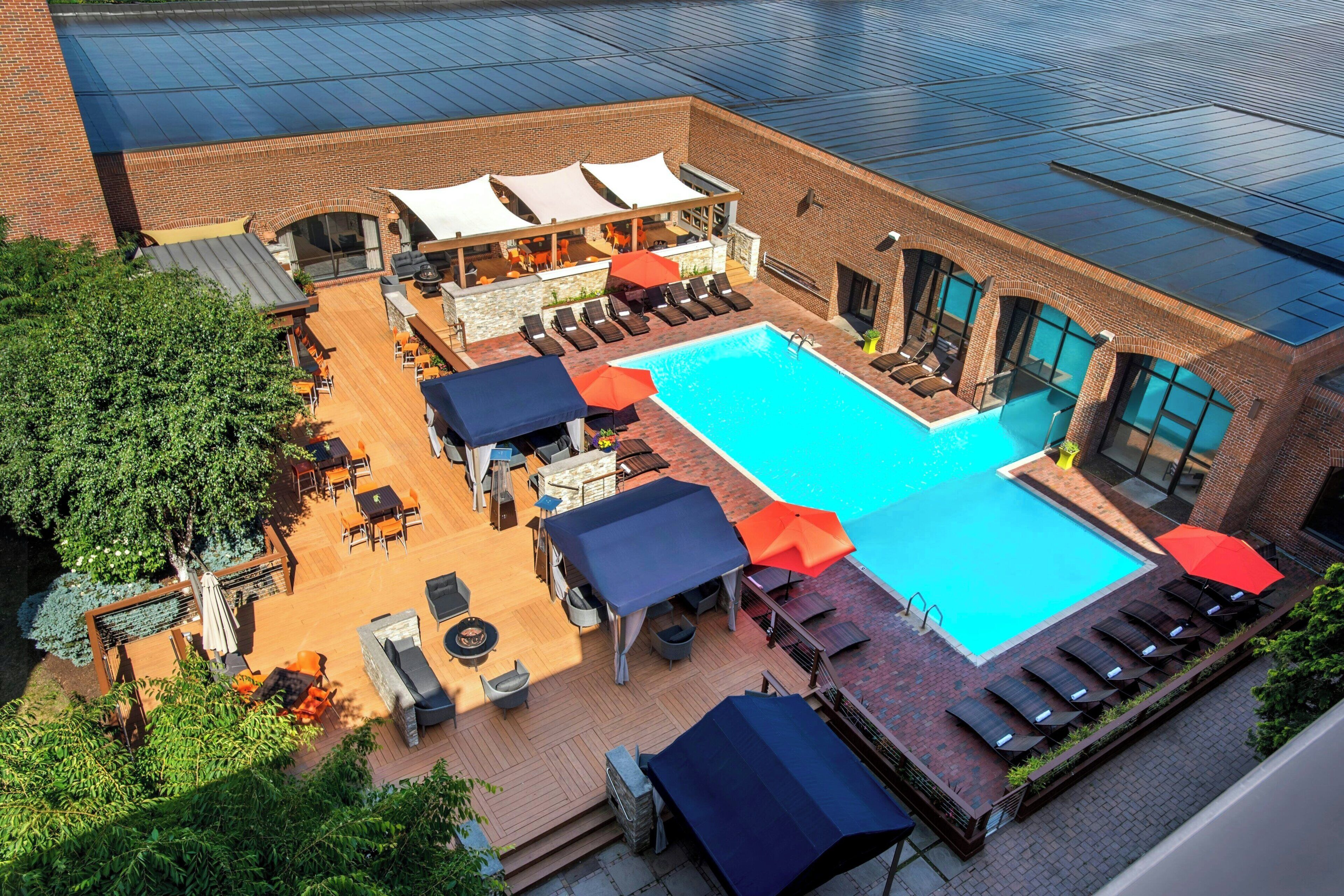 A rooftop pool area with lounge chairs, umbrellas, and a swimming pool.