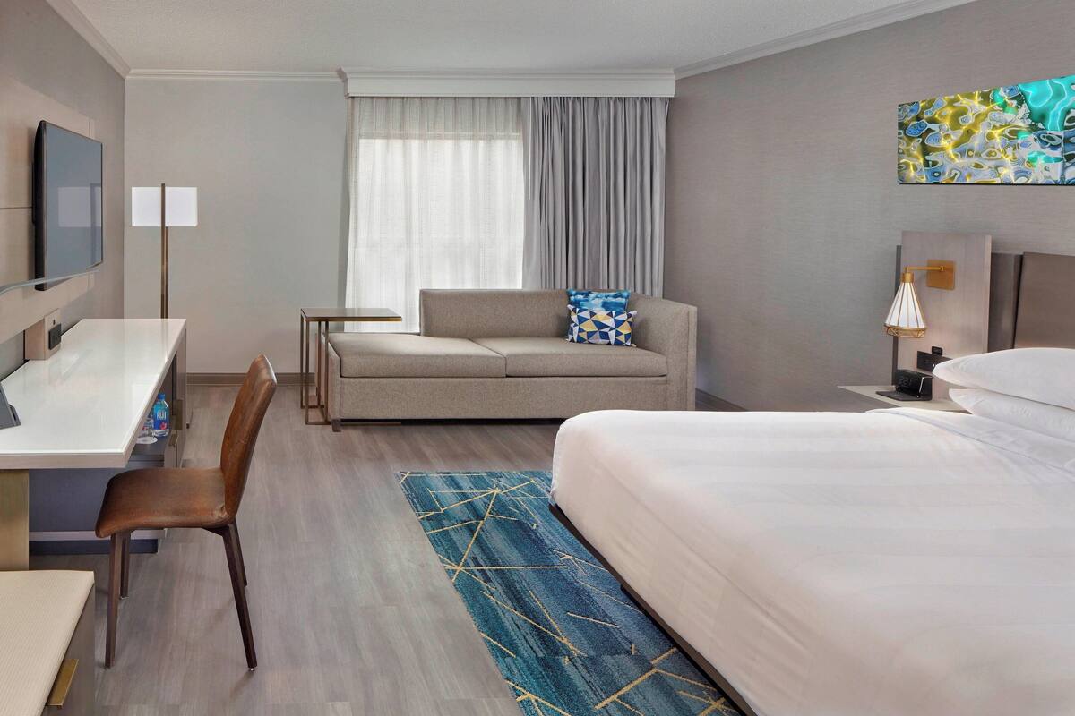 A hotel room with a bed, a sofa, a desk, and a TV.
