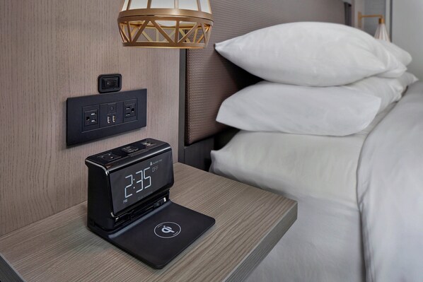 A modern hotel room with a bedside table featuring a digital clock and a power strip.