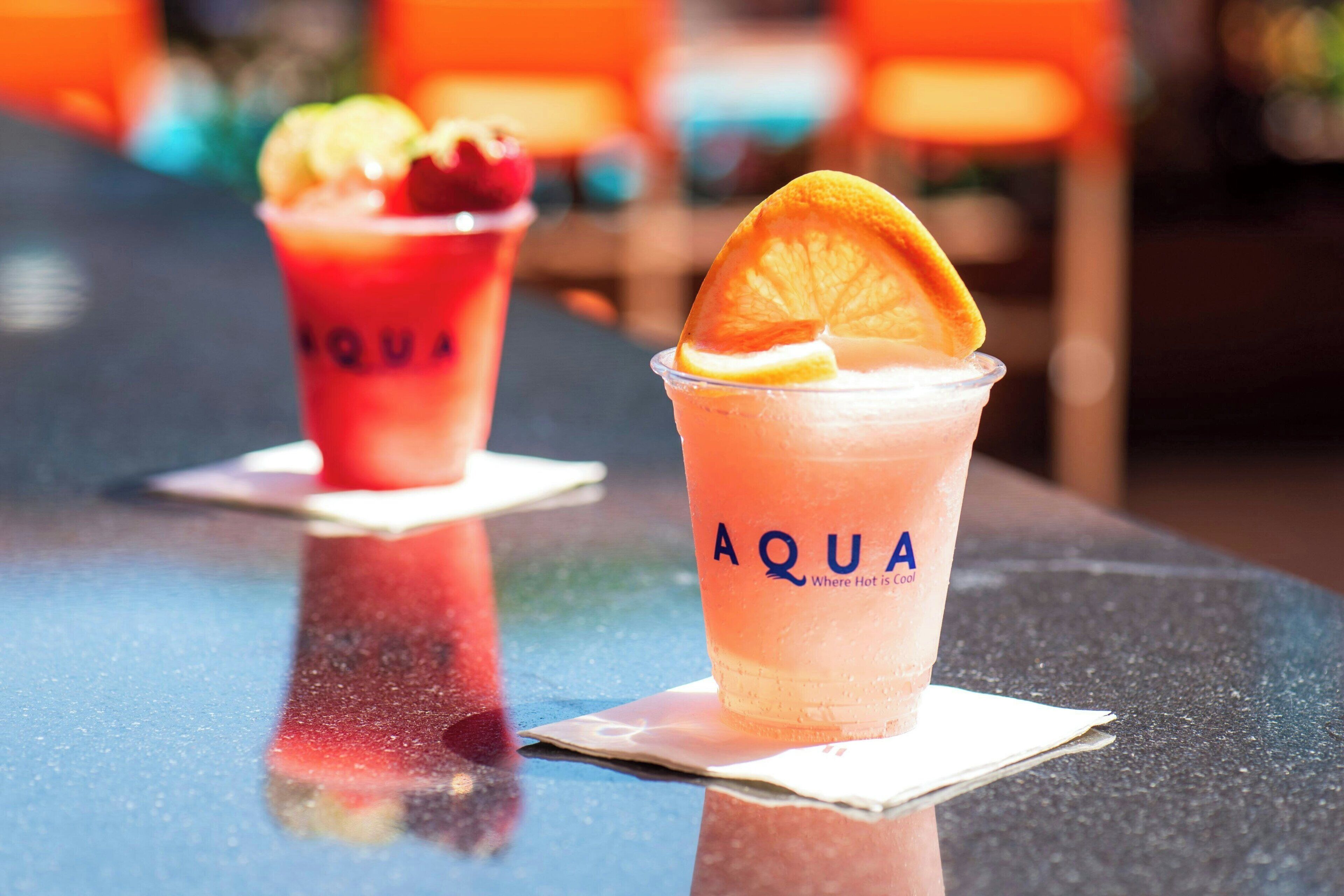 Dos bebidas con la marca 'AQUA' sobre una superficie reflectante, posiblemente una barra.