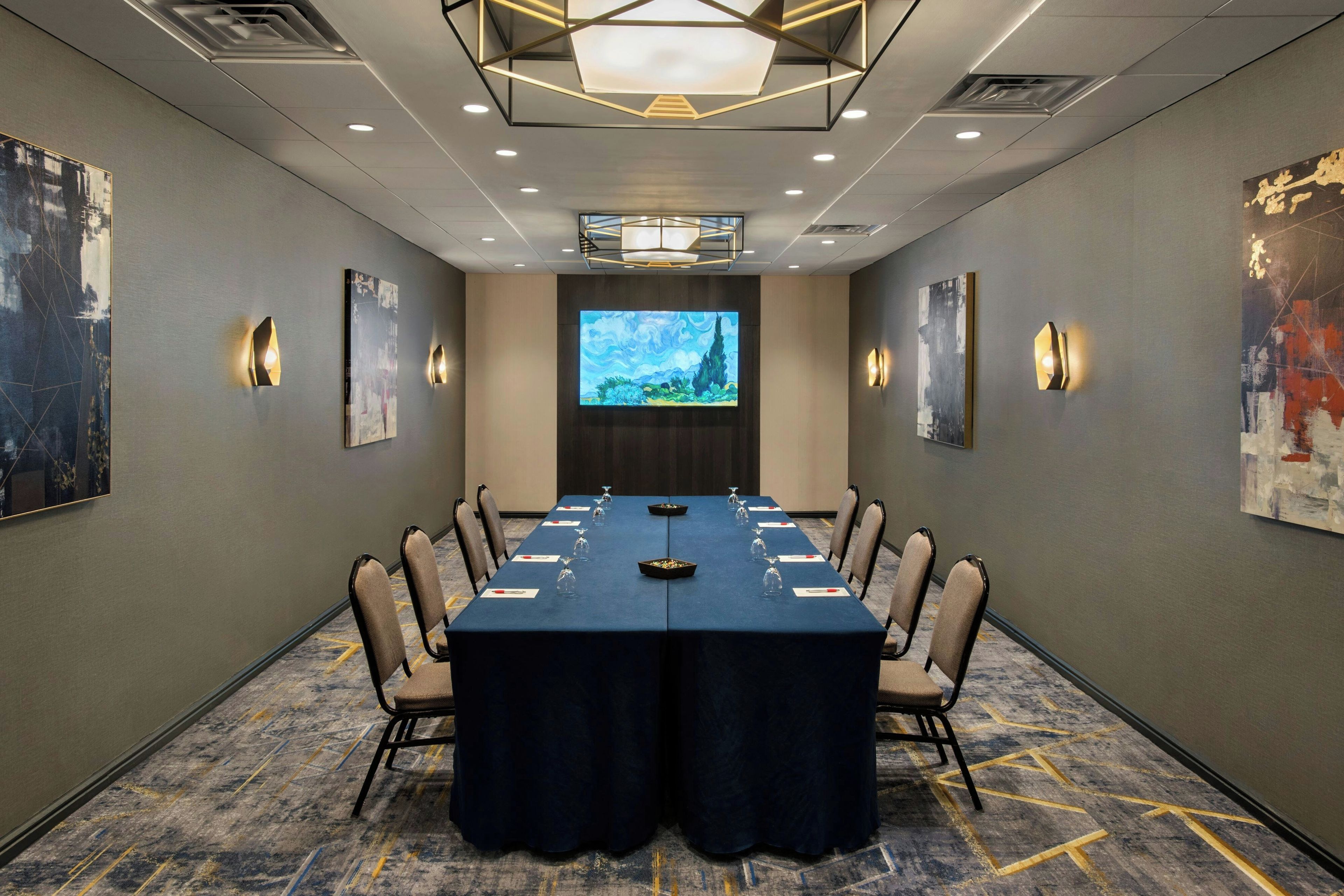 A conference room with a long table, chairs, and a screen at the front.